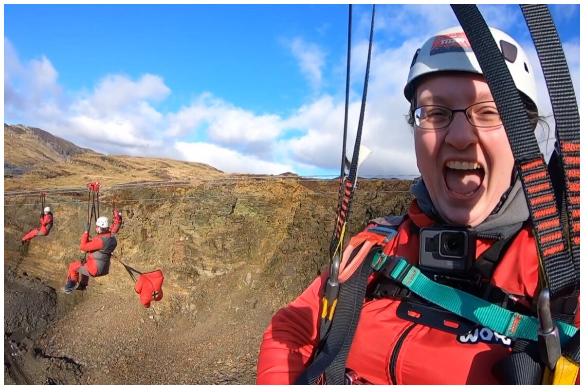 A photo of me (on the right) on Zipworld Titan's Bravo line. In the background is my husband and his parachute and behind him is the mountain and blue sky.
