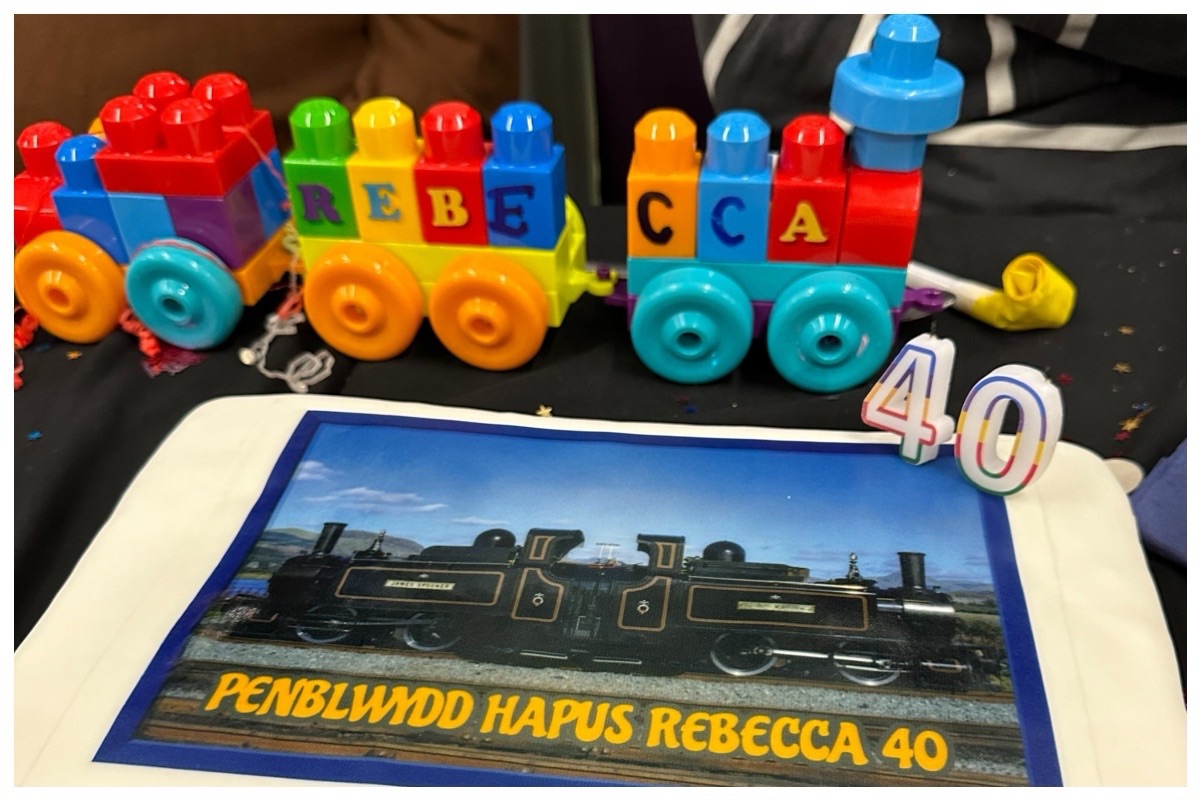 Plastic toy train and a cake saying happy birthday Rebecca (in Welsh)